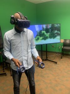 student wearing VR goggles and holding controllers in front of screen showing stanley park immersive experience